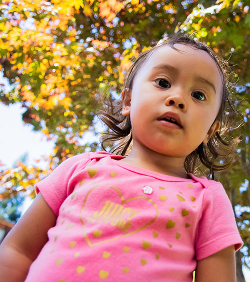 A young girl in a pink shirt stares down at the camera.