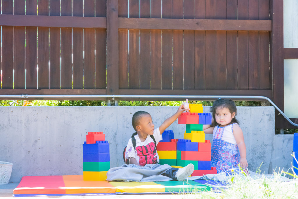 Two children play outside with oversized interlocking blocks.