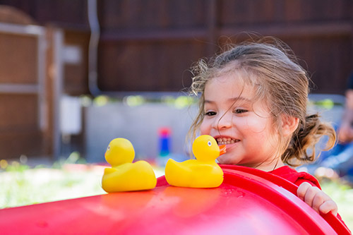 A child smiles while staring at two rubber duckies.