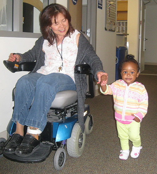 A woman in a mobility scooter holds the hand of a young child.